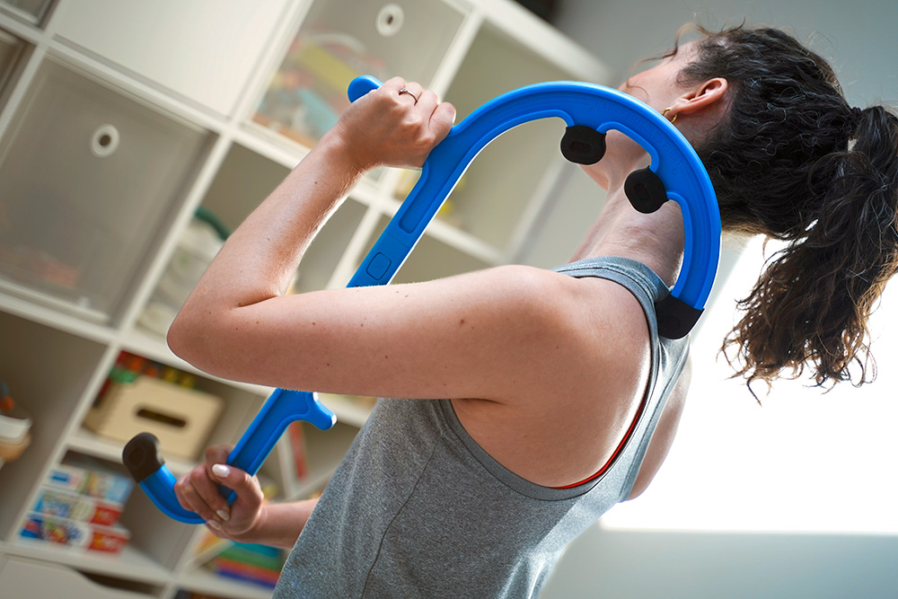 A person uses one of the best myofascial release tools massage hook like the Tiger Cane to massage muscle knots in the back, specifically targeting a painful knot in the shoulder blades for best myofascial release therapy.