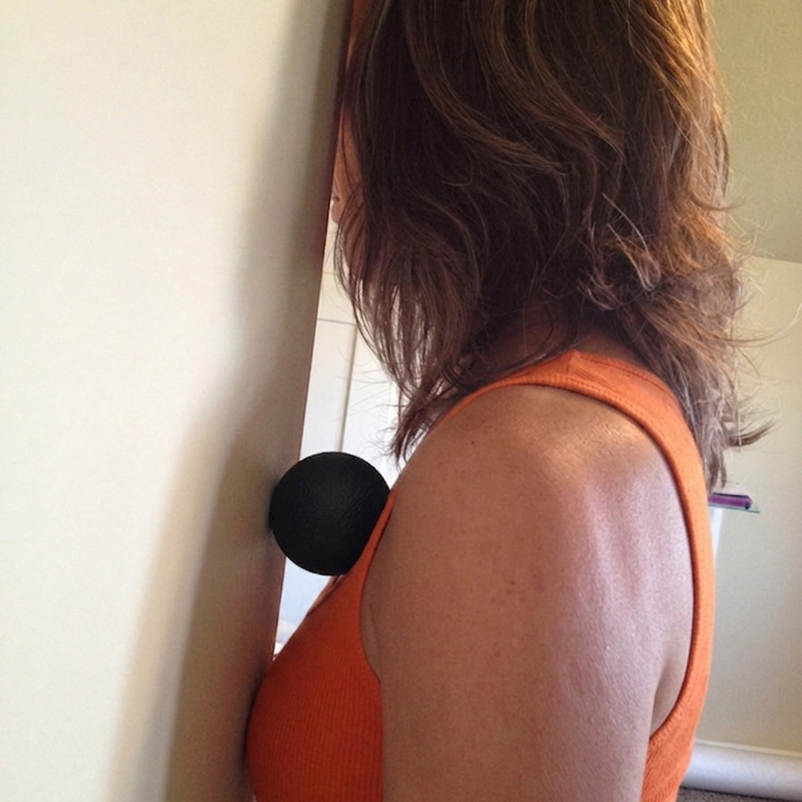 A woman massaging her pectoral minor muscle (upper chest) against a wall with Tiger Ball